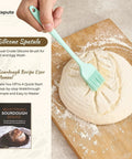 Hand brushing dough on cutting board with silicone spatula from Complete Sourdough Starter Kit With 9-Inch Round And 10-Inch Oval Banneton Proofing Baskets Plus 7 Essential Tools For Home Bakers Lame With 5 Blade Guard Bench Scraper Whisk Silicone Spatula Pastry Brush Bread Sling And Bag.
