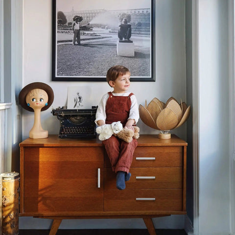 Child sitting on vintage mid-century modern sideboard with typewriter, doll head, and lotus lamp, framed photo above.