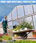 Man pushing wheelbarrow with plants in front of a greenhouse for fruit and vegetable protection