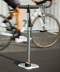 Bike Floor Pump With Industrial Gauge, Durable Aluminum Barrel Up To 160 Psi, 9 Inch Steel Base, Kraton Grips next to cyclist