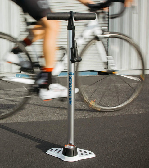 Bike Floor Pump With Industrial Gauge, Durable Aluminum Barrel Up To 160 Psi, 9 Inch Steel Base, Kraton Grips next to cyclist
