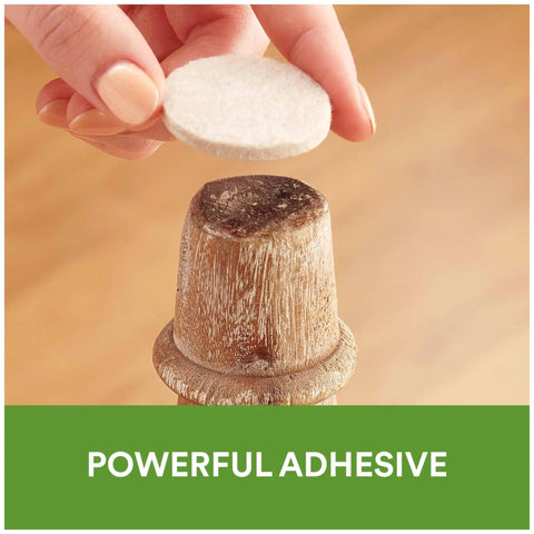 Applying beige 1-inch felt pad with self-stick adhesive to wooden furniture leg for floor protection from nicks and scratches.