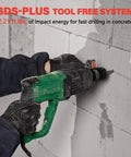 Side view of green Deshuo 1-inch SDS-Plus rotary hammer drill, corded, drilling into concrete with gloves.
