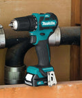 Ultra Compact 12V Max CXT Brushless Cordless Driver Drill resting beside plumbing, showcasing its compact size and design.
