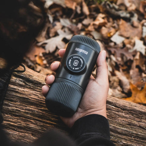 Hand holding Nanopresso Portable Espresso Maker With 18 Bar Pressure Manual Battery Free Travel Coffee Kit For Rich Crema On The Go Evolution From Minipresso Compact Grey in outdoor setting.