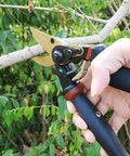 Hand holding 8.5 Inch Rotating Bypass Pruning Shears With Titanium Coated SK5 Blade cutting a thick branch.