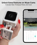 Expandable 32GB MicroSDHC Card Class 10 UHS-I U1 being inserted into a Wyze Cam with smartphone app interface displayed.