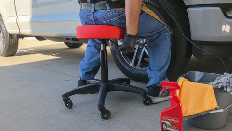 Rolling Shop Stool With Adjustable Height For Mechanics Padded Garage Seat With Smooth Rolling Wheels And ABEC Bearings Model 240250 Red in use next to a car wheel