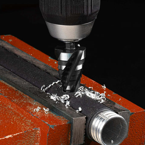Close-up of THINKWORK four-spiral-flute step drill bit in a drill chuck cutting into metal clamped in a vise, shavings.