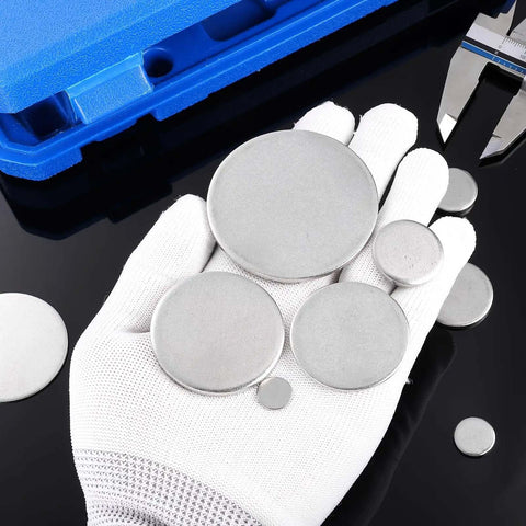 Gloved hand holding various sizes of stainless steel disc blanks, including Stainless Steel Disc Blanks For Engraving Five Eighths Inch Diameter 0.08 Inch Thick Round Metal Stamping Blanks Pack Of 55 For DIY Jewelry, Name Tags, Keychains And Crafts, on a black background with blue case.