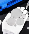Gloved hand holding Stainless Steel Round Disc Blanks 30mm Diameter 4mm Thick Engraving Ready 12 Pack Great For Jewelry Tags Keychains Badges DIY Crafts Personalized Signs And Metal Art Projects, with caliper and blue box nearby.