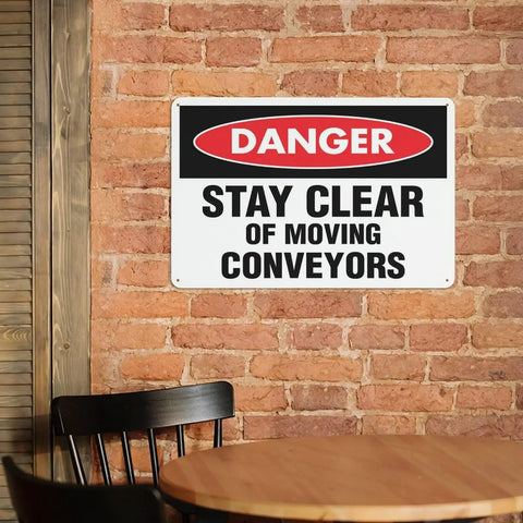 Stay Clear of Moving Conveyors Industrial Warning Sign 8 By 12 Inches Aluminum Wall Decor on brick wall near a wooden chair and table.