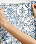 Hands applying blue Mediterranean tile peel and stick wallpaper no mess no water no fuss removable and repositionable.