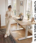 Woman enjoying coffee at a CubiCubi 55 x 28 electric standing desk in rich maple finish, perfect for home office comfort.