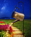 Solar Powered Watering Can Lantern Lights For Garden Decor hanging from hook illuminating flower pathway at night