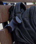 Chain Link Fence Hook For Sports Bags With Paracord Lanyard Heavy Duty Fence Hanger holding a black backpack on a brown bench