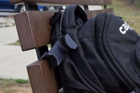 Chain Link Fence Hook For Sports Bags With Paracord Lanyard Heavy Duty Fence Hanger holding a black backpack on a brown bench