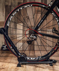 Foldable Bike Stand Floor Rack For MTB And Road Bikes With Quick Fold Design Durable Portable Garage Storage Fits Up To Two Point Four Inch Tire Width Easy Push In Front Holder Sturdy Bike Parking Rack shown holding a black bicycle tire