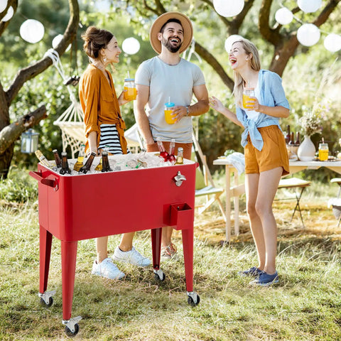 Three people enjoying drinks around a red 80 Quart Rolling Ice Chest Cooler On Wheels With Bottle Opener, Cap Catcher, And Bottom Storage Shelf.