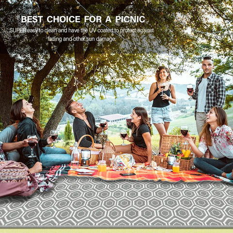 Group enjoying a picnic on a 9x18 Reversible Outdoor Camping Rug Weatherproof Patio Mat For RV Beach Backyard Deck And Picnic Two Gray And White Patterns Flip For A Fresh Look In An Instant, surrounded by trees.