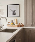 Precept Single Handle Kitchen Faucet With Side Sprayer in stainless, installed on a modern countertop, with a wicker basket and decor.