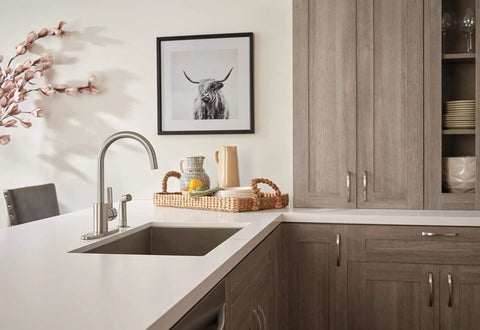 Precept Single Handle Kitchen Faucet With Side Sprayer in stainless, installed on a modern countertop, with a wicker basket and decor.