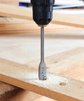 Spade drill bit in drill chuck drilling into a wooden board with sawdust