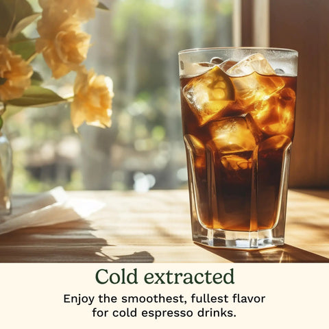 A glass of iced cold-extracted espresso on a wooden table with flowers in the background, highlighting a refreshing espresso drink.