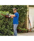 Person using 40V MAX Cordless Hedge Trimmer with 24 Inch Dual Action Blade, No Cords Needed, in a garden, cutting a hedge.