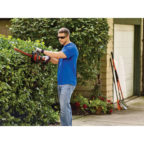 Person using 40V MAX Cordless Hedge Trimmer with 24 Inch Dual Action Blade, No Cords Needed, in a garden, cutting a hedge.