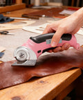 Heavy Duty Cordless Electric Scissors With Fast Usb Rechargeable Power And Self Sharpening Steel Blades For Slick Cuts Through Denim Fabric Leather Carpet And Stubborn Cardboard In Nifty Pink cutting brown leather on worktable.
