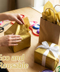 Person wrapping gifts with Gold Metallic Tissue Paper Pack 100 Sheets 14 By 20 Inches For Gift Bags And Wrapping Perfect For Birthdays