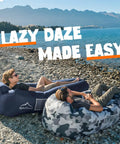 Two men relax on Inflatable Lounger Beach Chair With Air Sofa Hammock For Camping And Backyard Hangout on a lakeside beach.