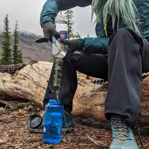 No Sweat Premium Grade Personal Water Filter Straw Camo 6 Pack Portable Purification Tube in use with blue water bottle outdoors.