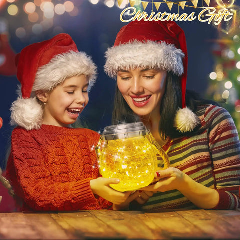 Mother and daughter with Christmas hats holding solar lantern glowing warmly indoors