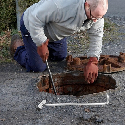 Person using Heavy Duty Stainless Steel Manhole Cover Hook With Sturdy T Shaped Handle Design For Dead Simple Storm Drain Grate Lifting.