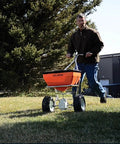 Man using Heavy Duty 70 Pound Spreader with Stainless Steel Frame on grassy lawn, showcasing precision and accuracy, sturdy design.