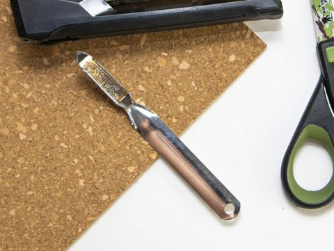 No-Tear Push-Style Staple Remover With All-Metal Chrome Construction, shown on cork surface with scissors in view