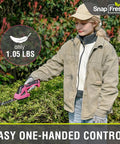 Slick Cordless Hedge Trimmer And Grass Shears 2 In 1 Lightweight Electric Bush Tool With Rechargeable Battery And Type C Charging Cable For Easy Peasy Trimming No Sweat Garden Cleanup Kit Pink held by user using one hand in a garden.