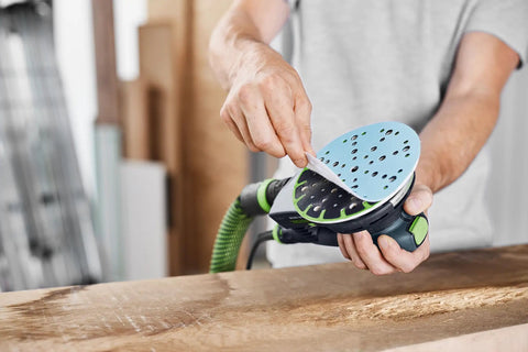 Person applying 80 Grit Granat Sanding Discs For 6 Inch Sander 50 Pack With Multi Jetstream 2 to a power sander on wooden surface.