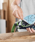 Person attaching Granat 100 Grit 6 Inch Sanding Discs for Orbital Sander to tool, focusing on abrasive surface for smooth finish.