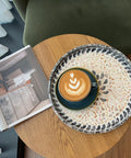 12 Inch Wooden Lazy Susan With Mother Of Pearl Inlay Smooth Spinning Turntable Serving Tray with a coffee cup on a wooden table.