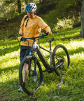 Person in orange shirt walking mountain bike downhill on grassy trail with helmet, showcasing Two Pack 27.5 Inch Heavy Duty Bike Tubes.