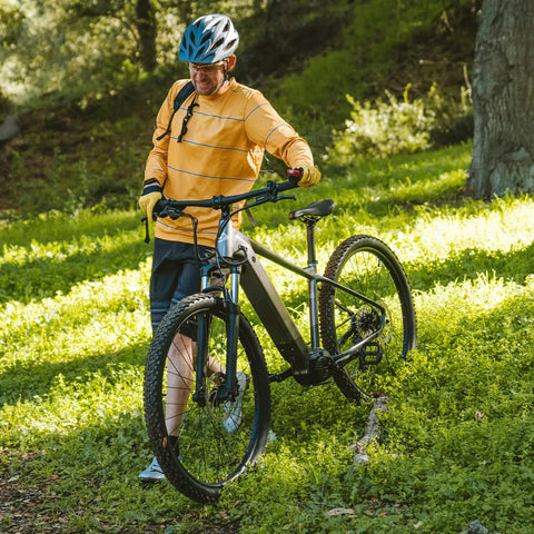 Person in orange shirt walking mountain bike downhill on grassy trail with helmet, showcasing Two Pack 27.5 Inch Heavy Duty Bike Tubes.