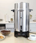 100 Cup Commercial Coffee Urn With Automatic Temperature Control Fast Brewing Easy Clean Up NSF Approved Large Capacity Keeps Joe Hot All Day Silver For Large Events, shown on a countertop with coffee and snacks.