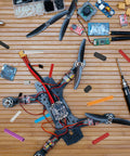 Quadcopter drone frame with carbon fiber arms, motors, and wiring on a wooden workbench.