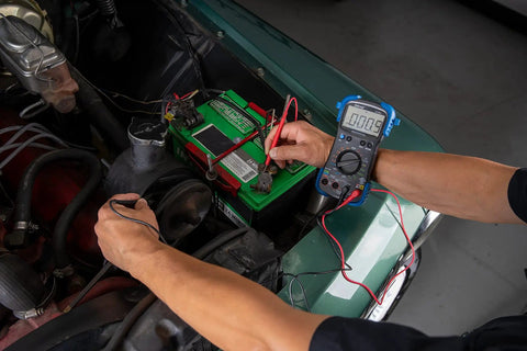 Person using Pro Grade Automotive Digital Multimeter With Auto Range And Overload Protection Measures Up To 15 Amps 10 MOhm Input Impedance Auto Shutoff Tests Diodes Duty Cycle Solenoids Wiring And Switches For Engine Diagnostics on car battery