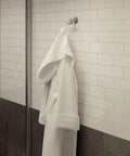 Wall-mounted robe hook from the Elm 4 Piece Wall Mounted Bathroom Hardware Set in Satin Nickel, holding a white robe.