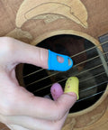 Close-up of fingers with colorful finger picks on guitar strings from Guitar Maintenance Kit 77 Piece Set With Carry Bag For Acoustic Electric Ukulele Bass Banjo And Other String Instruments Includes Nut Saddle Files Radius Gauges Allen Wrenches Bridge Pins Winder Pliers Feeler Gauge And More For Quick Pro Setups.