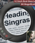 Close-up of 8X Magnifying Glass With Light Floor Lamp For DIYers showing a 4.3-inch lens magnifying text on a newspaper page.
